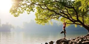Person practicing yoga by peaceful water in nature.