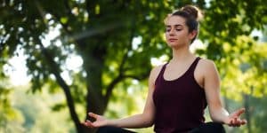 Person meditating peacefully outdoors, sun shining.