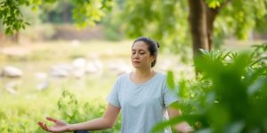 Calm person meditating peacefully outdoors with serene nature background.